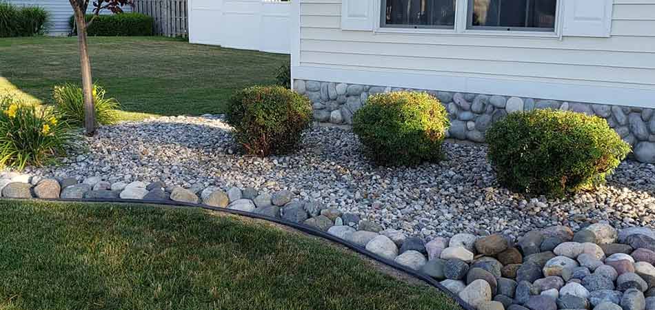 Well maintained landscape bed in Midland, MI with decorative rocks and trimmed plants.
